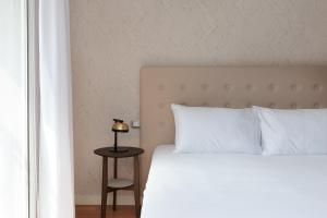 a bed with white pillows and a table with a lamp at Portopiccolo Apartments Deluxe in Sistiana