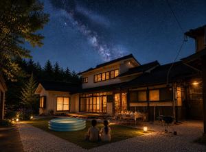 two people sitting in front of a house at night at 貸切り200m2 林檎のワルツ 広い和モダン邸宅 星空とBBQ in Komoro