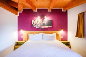 a bedroom with a white bed with a purple wall at Residenza Garibaldi - Cirmolo in Molveno