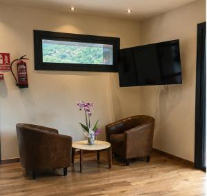 ein Wohnzimmer mit zwei Stühlen und einem Tisch und einem Fernseher in der Unterkunft XIA Hotel Boutique in Rialp