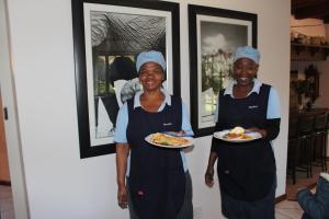 two women in aprons holding plates of food at Bayside Lodge Garden Route B&B in Plettenberg Bay +60 photos