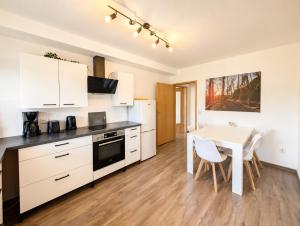 a kitchen with white cabinets and a white table and a table and chairs at Urlaubsmagie Ferienwohnung Wiesengrün - direkt am Wanderweg - für 6P - W6 in Sebnitz