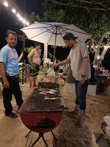 a man cooking food on a grill with an umbrella at Chomlay House in Ban Thepha