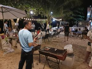 a man cooking food on a grill on the beach at Chomlay House in Ban Thepha