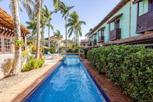 a pool in front of a house with palm trees at Pousada Lua Chalés in Maresias
