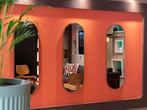 an orange wall with two mirrors in a living room at Novotel Paris Rueil Malmaison in Rueil-Malmaison
