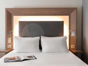 a bed with two pillows and a book on it at Novotel Paris Rueil Malmaison in Rueil-Malmaison