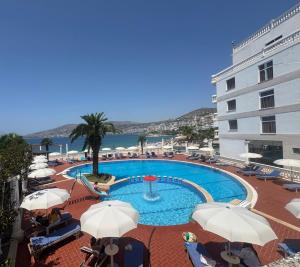 a swimming pool with umbrellas and chairs and a building at Hotel Dodona in Sarandë