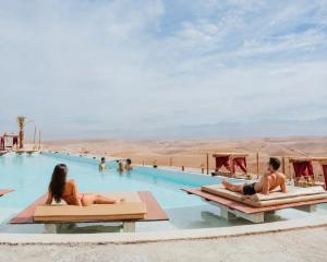a group of people laying on beds in a swimming pool in the desert at Sunset Agafay Resort in El Karia