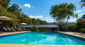a swimming pool with chairs and trees in the background at Vila Francesa Hotel in Penedo