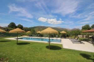 a pool with straw umbrellas and chairs and tables at Casa do Mestre by Gerês Casas in Geres