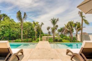 a swimming pool with two chairs and palm trees at Chic Beachfront Condo Ocean View Rooftop Pools in Akumal