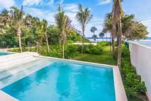 a swimming pool with palm trees and the ocean at Chic Beachfront Condo Ocean View Rooftop Pools in Akumal