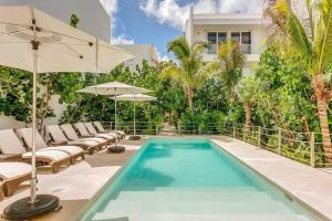 a swimming pool with lounge chairs and an umbrella next to a house at Chic Beachfront Condo Ocean View Rooftop Pools in Akumal +27 photos