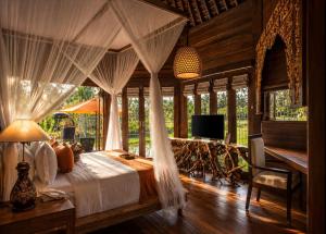 a bedroom with a bed with curtains and a television at Green Field Resort Ubud in Ubud