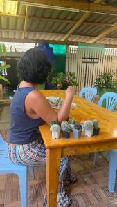 a woman sitting at a wooden table with cactuses at Baan Yuan in Prachuap Khiri Khan +4 photos
