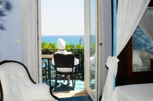 een vrouw in een stoel op een balkon met uitzicht op de oceaan bij Hotel Palladio in Giardini Naxos