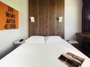 a bedroom with a white bed and a orange sign at ibis Styles Niort Poitou Charentes in Vouillé