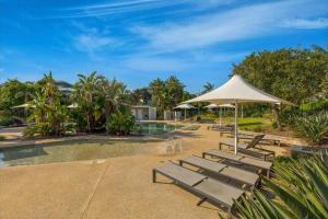 a group of benches and an umbrella next to a pool at 3BR Golfside Villa | Pools, Tennis & Relaxation in Magenta