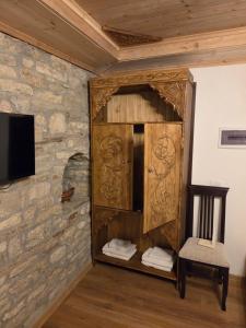 a wooden cabinet against a stone wall with a chair at Guri Guesthouse in Gjirokastër