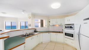 a kitchen with white cabinets and the ocean in the background at Pacific Waves Apartments in Noosa Heads