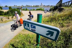 two people riding bikes on a road with a sign at Camping Port la Vallée in Saint-Mathurin
