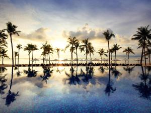 a pool with palm trees and the sunset in the background at Novotel Phu Quoc Resort in Phú Quốc