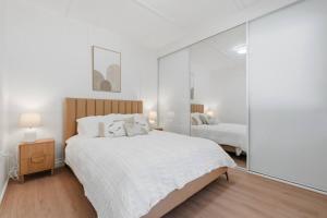 a white bedroom with a large bed and a mirror at Central Coast Waterfront 2BR with Jetty Access in Koolewong