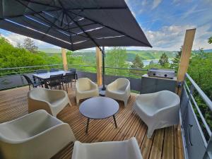 a deck with white chairs and tables and an umbrella at Les Reflets Verts - Lac de Vouglans in Maisod