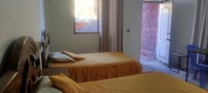 a bedroom with two beds and a window and a table at Hostal Cadena in Tupiza +6 photos