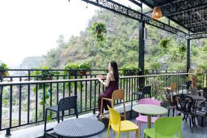 a woman sitting on a balcony with colorful chairs and tables at Cat Ba Vista Luxury Hotel - New 2026 - Rooftop Infinity Pool in Cat Ba