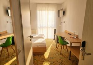 a room with a table and green chairs and a desk at Hotel AVIVA by APOLONIA in Karlsruhe