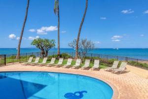 a swimming pool with chairs and the ocean in the background at Kihei Beach 606 - Direct Ocean Front, Central AC! in Kihei