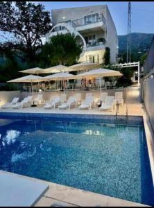a swimming pool with chairs and umbrellas next to a building at MostOliva luxury Rooms in Pržno