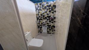 a bathroom with a toilet and a tile wall at Thuyil Inn Koodal in Madurai