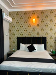 a bedroom with a bed with a black headboard and a wall at Oasis Family Hotel in Lahore