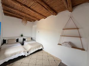 two beds in a room with white walls and wooden ceilings at Dar Isma : Une maison sur océan in Wassane