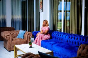 a woman sitting on a blue couch in a living room at CHROME Résidences Fidjrossè PLAGE in Cotonou
