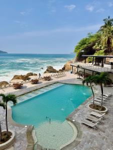 a swimming pool on the beach with chairs and the ocean at Suite Deluxe frente al Mar - Playa & GYM in Acapulco