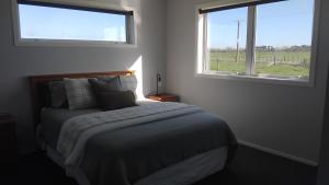 a bedroom with a large bed with two windows at The Quiet Paddock in Kairanga