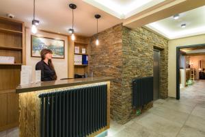 a woman standing at a counter in a lobby with a stone wall at Hotel Malé Versailles in Karlovy Vary