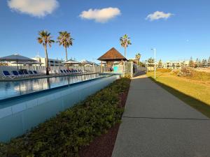 a walkway next to a swimming pool with palm trees at Mandurah Coastal Studio - Pool Outlook in Mandurah