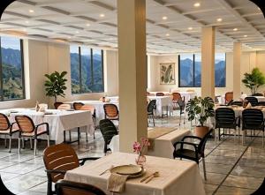a restaurant with white tables and chairs and windows at Kove Hotel & Resort in Naran