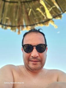 Ein Mann mit Sonnenbrille steht unter einem Regenschirm in der Unterkunft Riyadh palms in Constantine