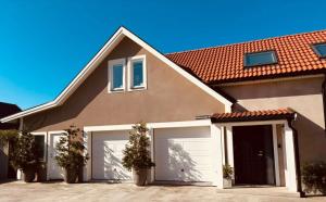 ein Haus mit weißen Garagentoren und einem roten Dach in der Unterkunft Kullsbacka in Skanör med Falsterbo