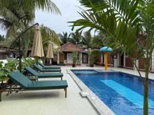 a pool with chairs and umbrellas next to a resort at Palm Escape Beach Resort in Baga