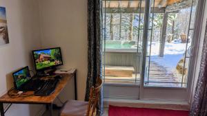 a desk with a laptop and a computer monitor and a window at Chalet Le Boisé SPA et Rivière in Brownsburg