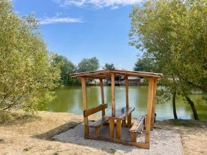 a picnic shelter with two benches in front of a lake at MAX Jazero in Trstice