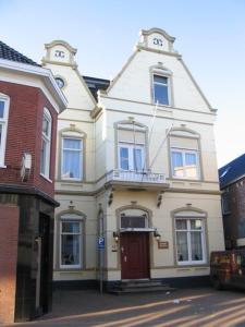 a white house with a red door on a street at Pension Delfzijl in Delfzijl