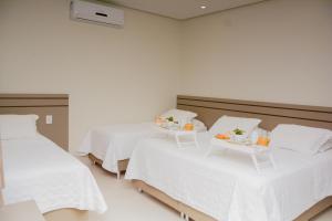a room with two beds with white sheets and fruit on tables at Hotel Imperador in Gurupi